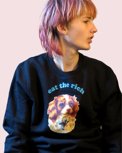 Person trägt Vintage-Illustration eines Cocker-Spaniel-Welpen mit ‚Eat the Rich‘ Typografie auf Eco-Sweater, Blick zur Seite