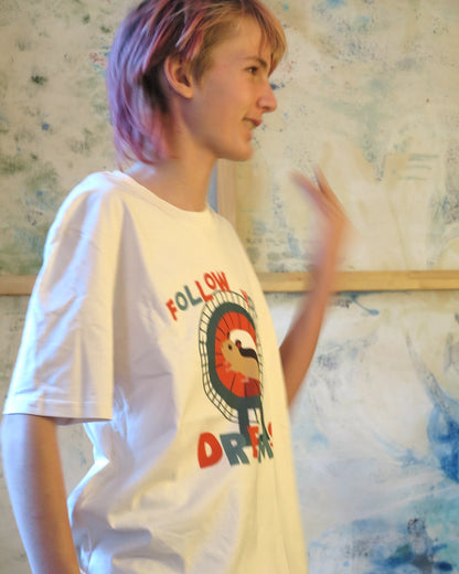 winkende Person trägt Illustration eines Hamsters im Laufrad mit der Typografie ‚Follow Your Dreams‘ im collageartigen Cartoon-Stil auf einem weißen T-Shirt, Seitenansicht