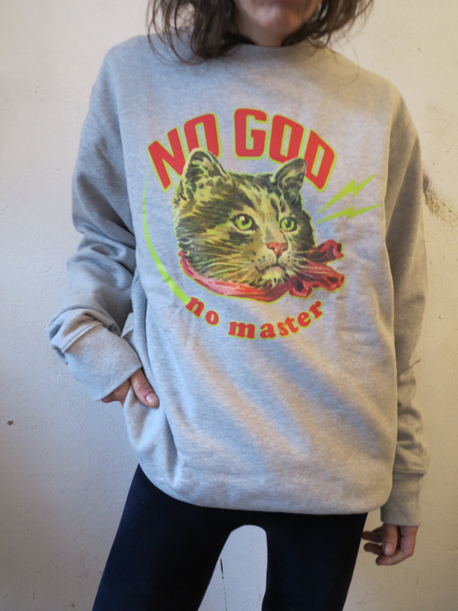 Person trägt Vintage-Porträt-Illustration einer Katze mit rotem Halstuch und dem Schriftzug ‚No God No Master‘ auf einem Sweater aus Bio-Baumwolle